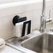 An image of the Happy Sinks Black Sponge Holder mounted in a kitchen, holding a sponge by the sink.