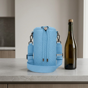 A blue textured leather champagne bag sits on a grey counter, dwarfed by a standard champagne bottle.