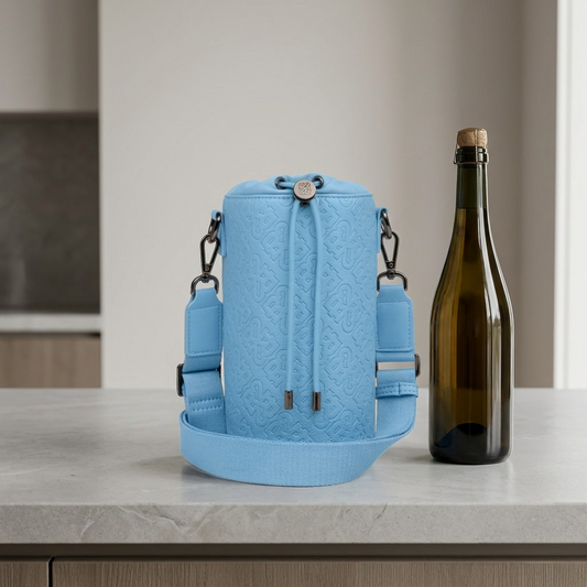 A blue textured leather champagne bag sits on a grey counter, dwarfed by a standard champagne bottle.