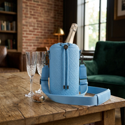 A close-up photograph of the blue quilted leather Bugatti champagne bag resting on a wooden table, featuring an open champagne bottle.