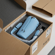 Unboxing of the blue leather bag, shown protected within foam inserts and an open shipping box.