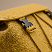 Extreme close-up of the textured leather and embossed logos on a yellow luxury backpack.