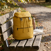 Lifestyle shot of Bugatti's Voltage Yellow backpack resting on a park bench beside a book and water bottle.