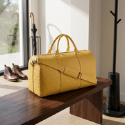 A realistic photo of the yellow textured Bugatti duffle bag placed on a modern, dark wood bench in a stylish, contemporary home entryway, with natural sunlight from an unseen window.