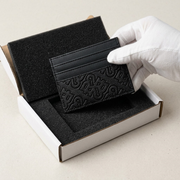 Unboxing: Black textured leather card holder revealed in secure foam-cut insert and protective box for safe delivery.