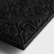 A macro photograph displaying the intricate, debossed signature motif pattern on the black PU material, featuring crisp stitching.