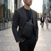 A man in a sleek black leather jacket carries the Bugatti sling bag as he walks down a city street, demonstrating its stylish functionality.