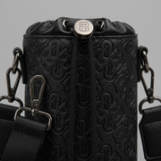 A detailed macro shot with realistic depth of field highlighting the embossed monogram PU black texture of the Bugatti Rick Ross Champagne Bag, focusing on the drawstring hardware and shoulder strap attachment points.