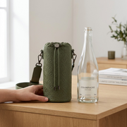 A lifestyle photo of the green Bugatti Rick Ross Champagne Bag, placed accurately beside a standard 750ml glass wine bottle to reference its compact, portable scale for carrying champagne. The clean, neutral ecommerce background is brand-aligned and features realistic lighting.