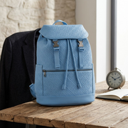 A low-angle lifestyle photo shows the blue Bugatti Rick Ross backpack on aged wood grain. A stone background, warm light. All features are precise.