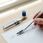 A close-up photograph of one Pentel 0.7mm Blue Refill Lead tube in use, lying on a wooden desk next to a sheet of graph paper and an open mechanical pencil, with other leads partially inserted. Natural light illuminates the scene, which emphasizes the fine line product in a working environment. An individual lead is shown resting on the paper, indicating it writes with blue.