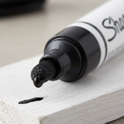 Macro detail of a black Sharpie oil-based paint marker bold point tip dispensing opaque black ink.