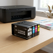 A lifestyle photo of the four-pack of Canon PGI-1200XL ink cartridges resting on a wooden desk next to a printer.