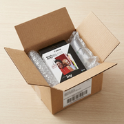 A Cannon logo box is shown secure and protected by bubble wrap and airbags inside a larger brown shipping container. Its ZINK Photo Paper 100-pack is nestled safely, reducing shipping fears.