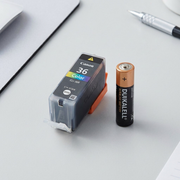 A photo of the single CLI-36 ink cartridge beside and slightly smaller than a standard AAA battery.