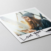 Close-up photo detailing a square SELPHY instant photo print with realistic grain, deep color, and handwritten text "Love you!", highlighting quality and personalization.