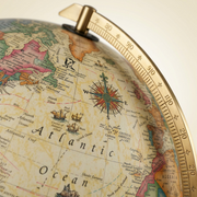 Macro photograph focusing on the detailed print of the antique-style map, gold-finish meridian, and a compass rose.
