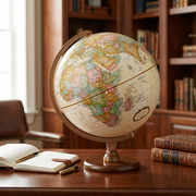 Lifestyle photo of the Replogle Hastings antique ocean desk globe on a dark wood study desk beside a leather notebook.