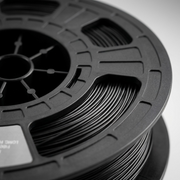 A detailed macro photograph showing the high-precision winds of 1.75mm black 3D Nylon filament on its matching spool, with complex geometric structures.